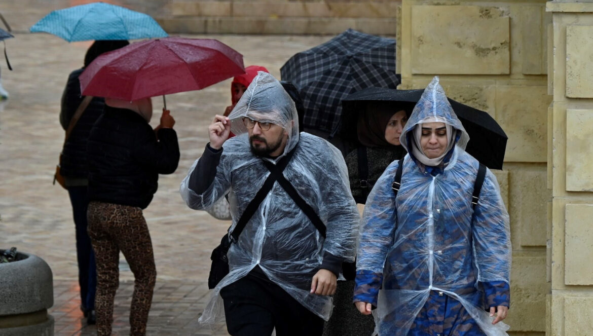 Varias personas caminan por el entorno del Puente Romano protegidos de la lluvia. / Juan Ayala