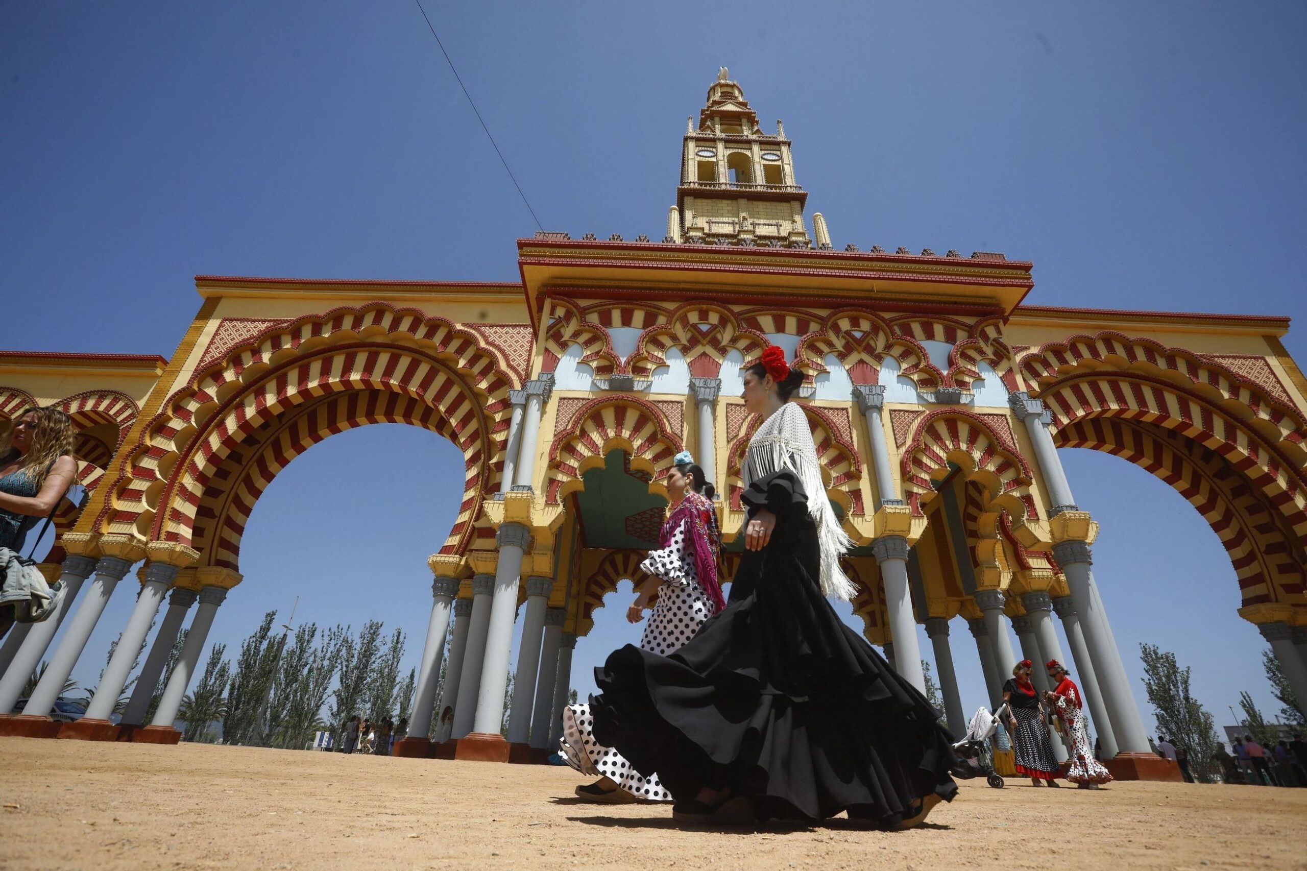 Mujeres con traje de flamenca, junto a la portada de la Feria de Córdoba. / Salas / Efe