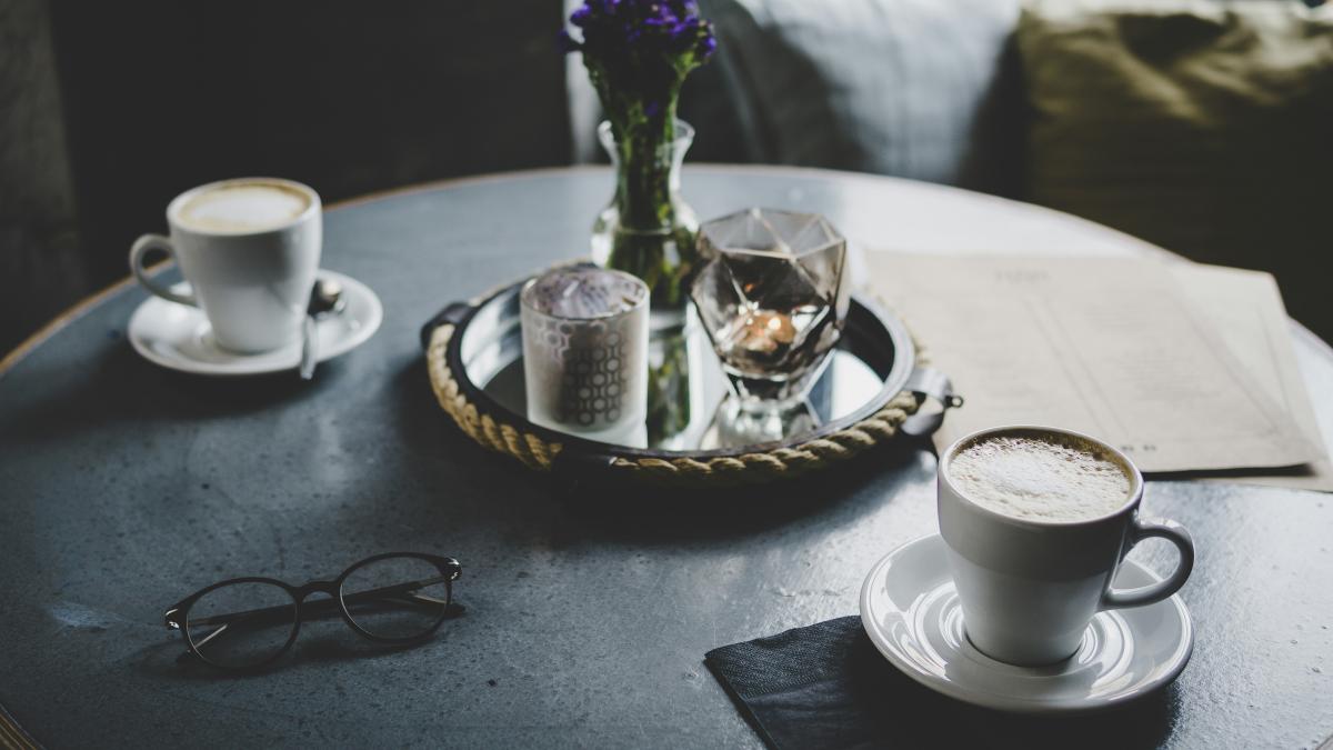 round tray with flower vase between two white ceramic teacups above table
