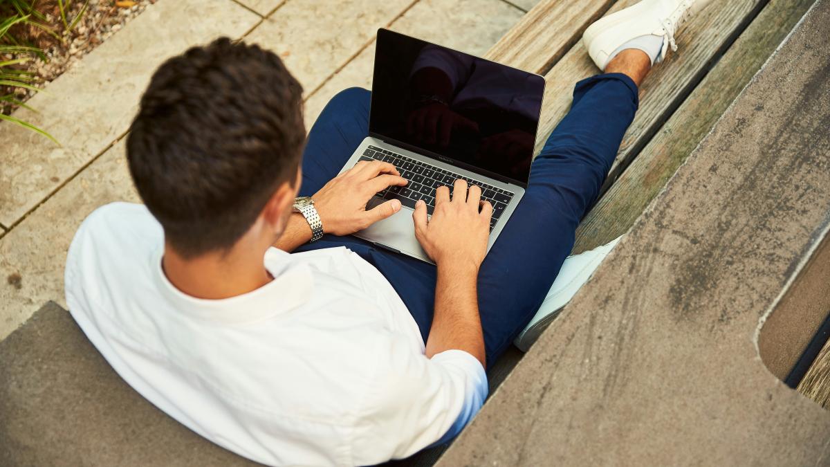 man wearing white sweatshirt using laptop computer sitting on sofa chair