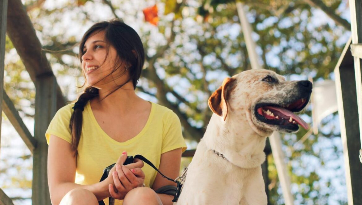 woman in yellow tank top sitting beside white short coated dog