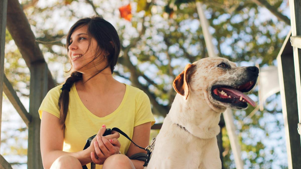 woman in yellow tank top sitting beside white short coated dog