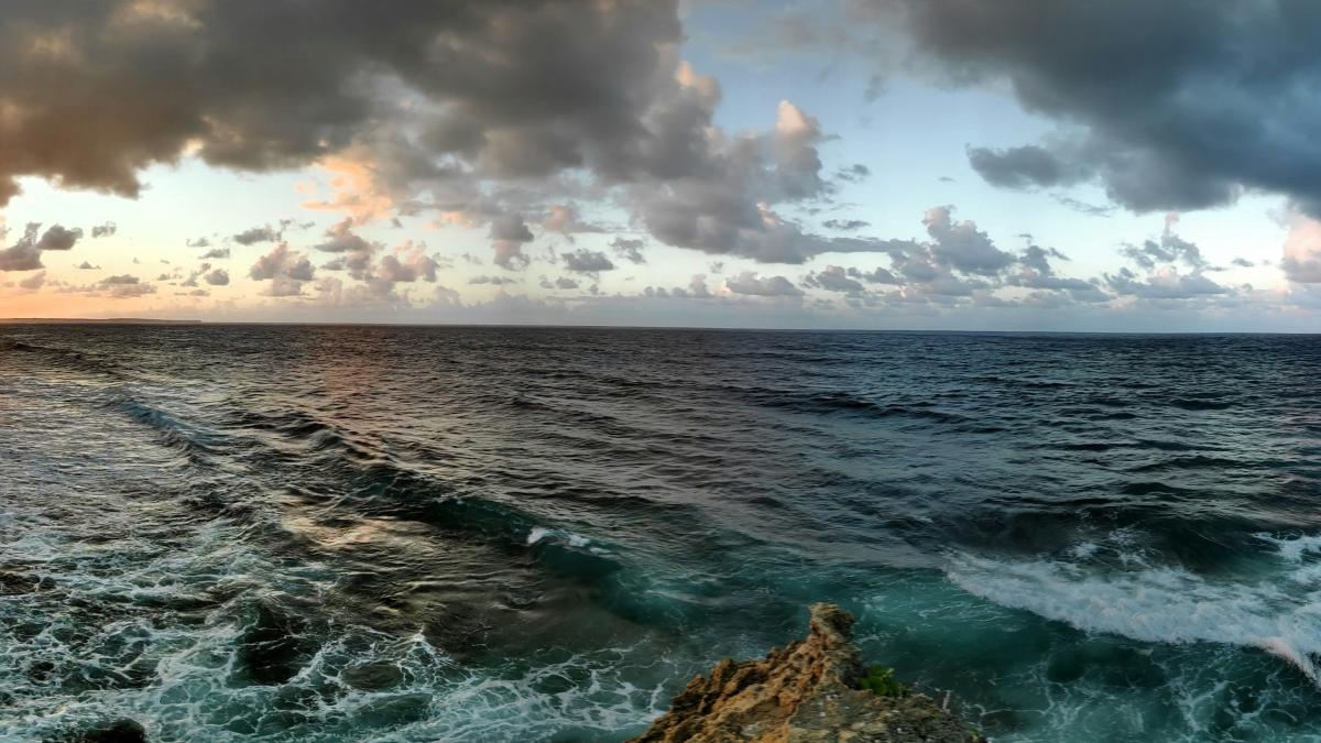 ocean waves crashing on brown rock formation under white clouds and blue sky during daytime