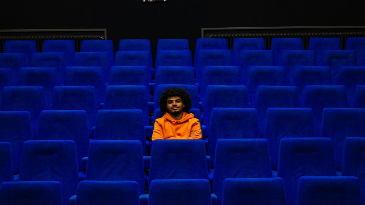 a man sitting in a blue chair in a theater