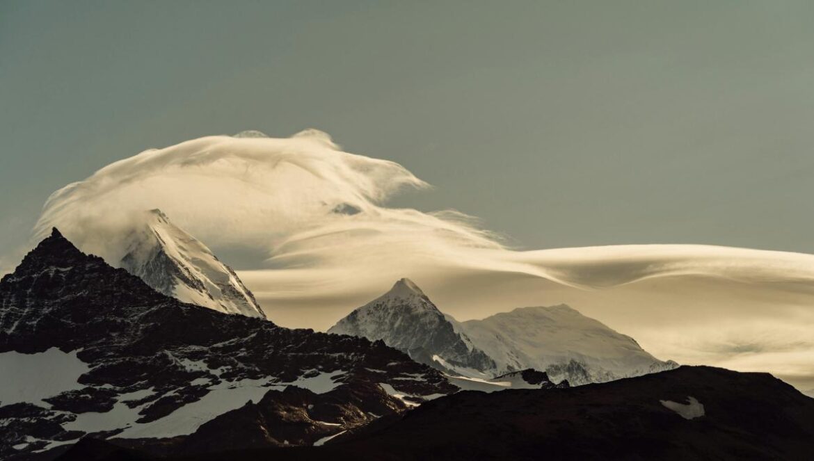 a mountain covered in clouds and snow under a blue sky