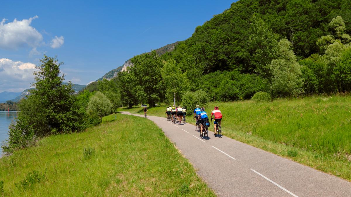 a group of people riding bikes on a road by a lake