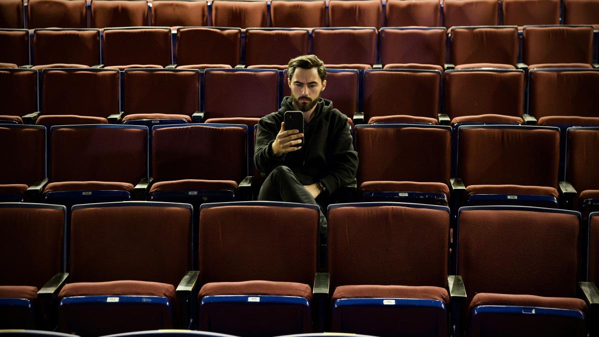 a man sitting in a theater looking at his cell phone