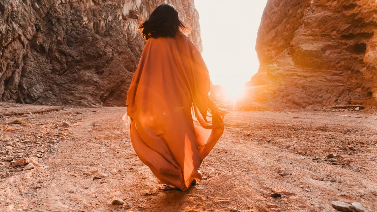 a woman in an orange dress walking through a canyon