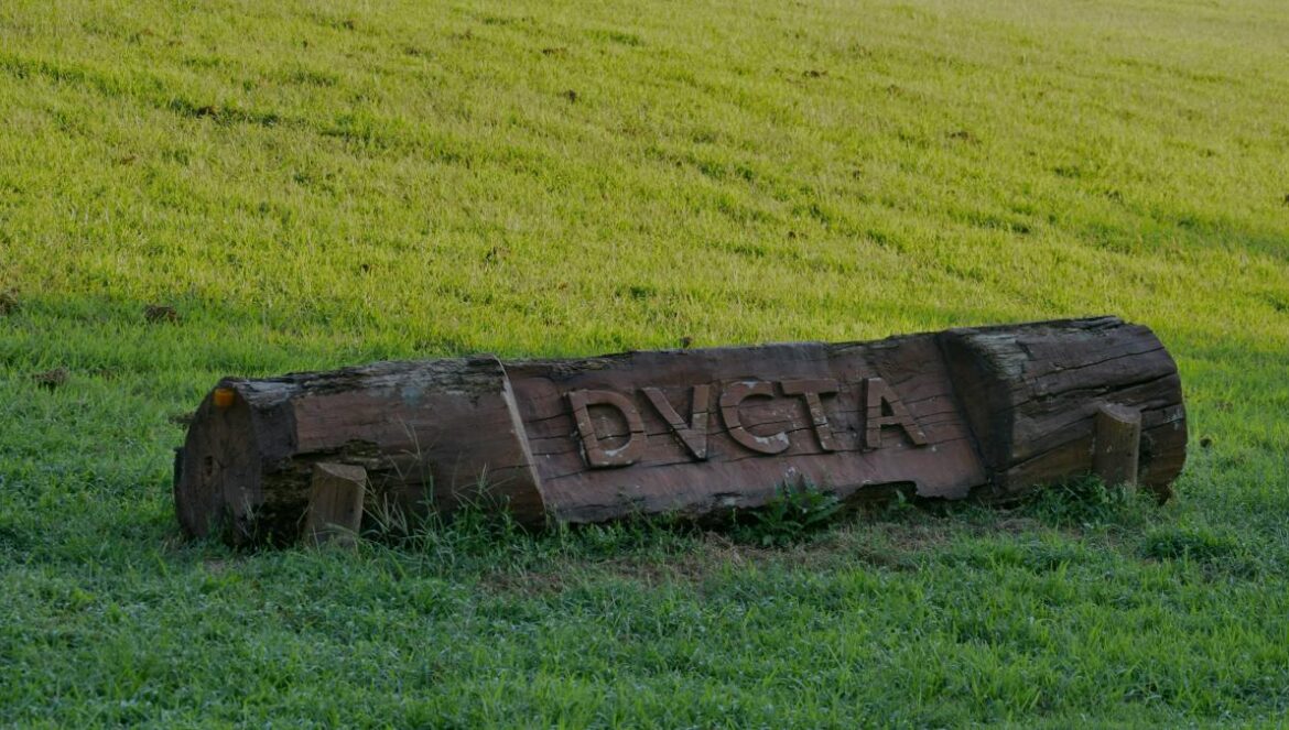 a wooden sign sitting in the middle of a lush green field