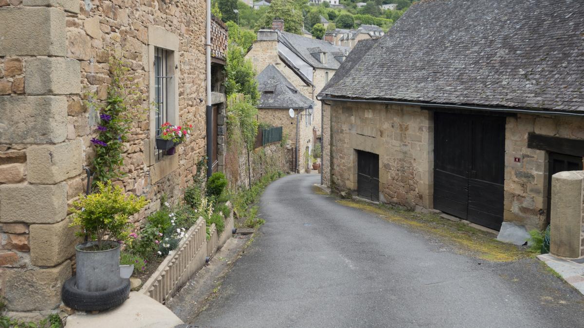 a narrow street with a stone building and a potted planter