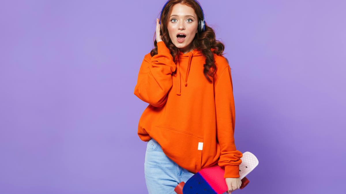 a woman in an orange sweatshirt is holding a skateboard