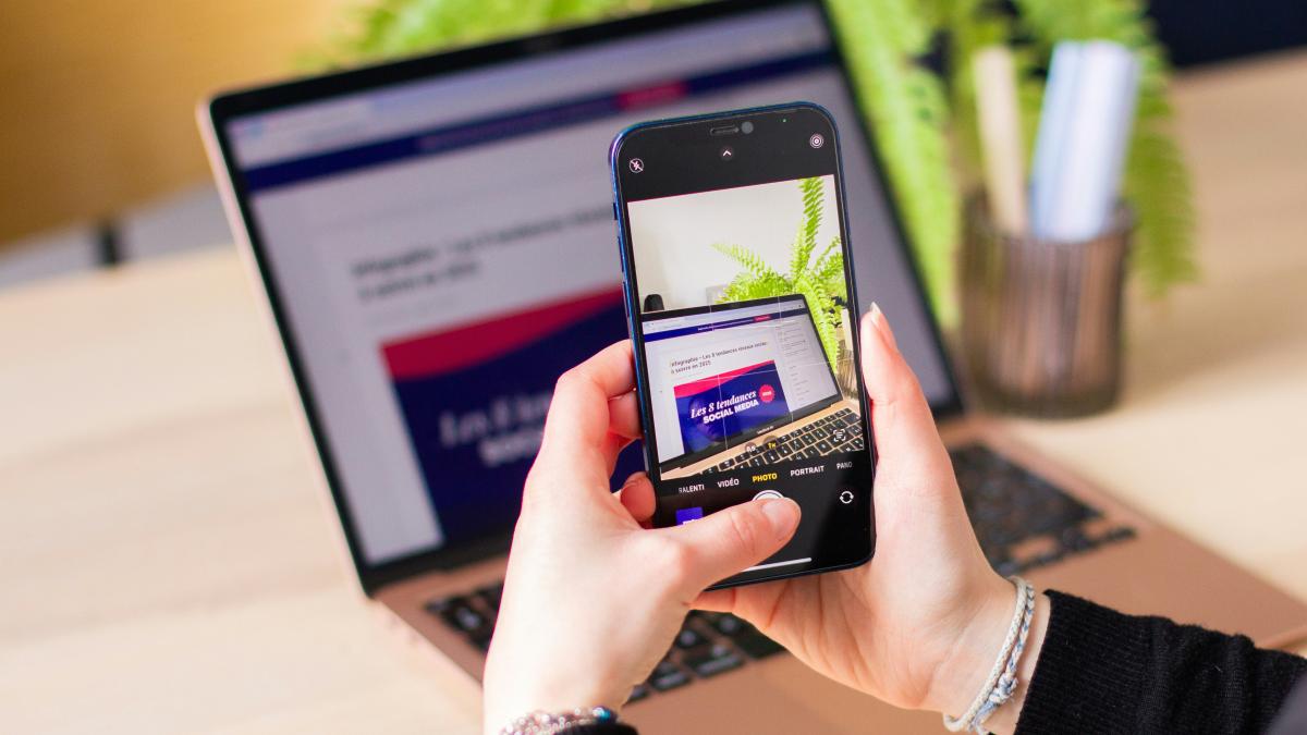 A person holding a cell phone in front of a laptop