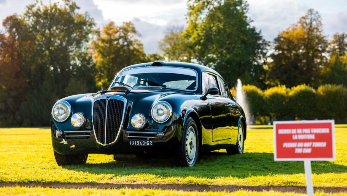 A classic black car parked on a grassy field.