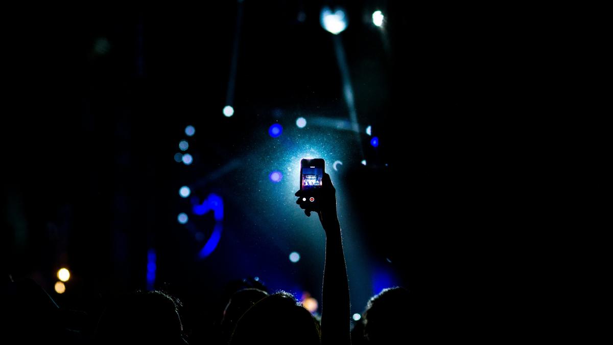 low light photography of person raising hand holding smartphone