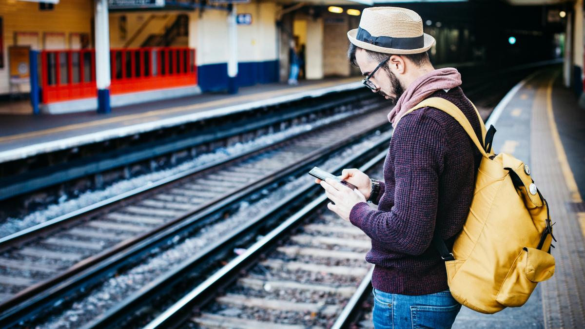 man using phone while standing in front of train rail during daytime