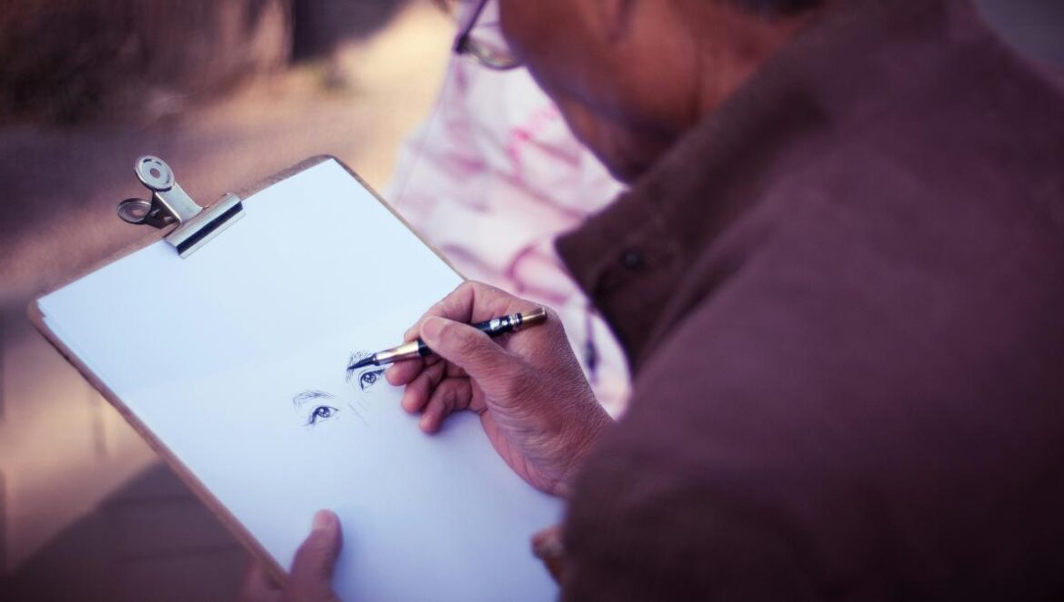 man sketching face on white printer paper