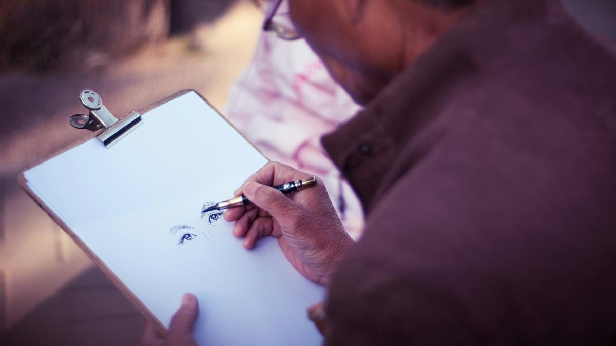man sketching face on white printer paper