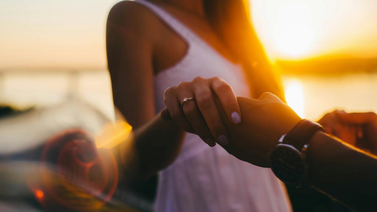 selective focus photography of woman wearing white sleeveless dress holding human hand during golden hour