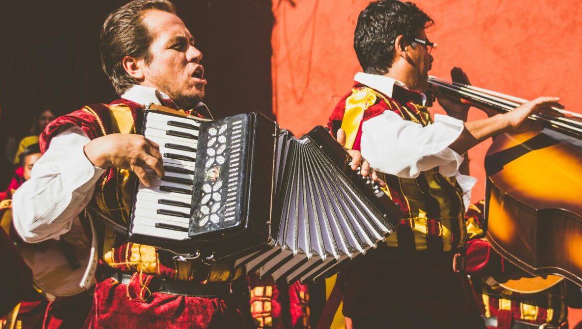 two men playing cello and accordion beside red building photo