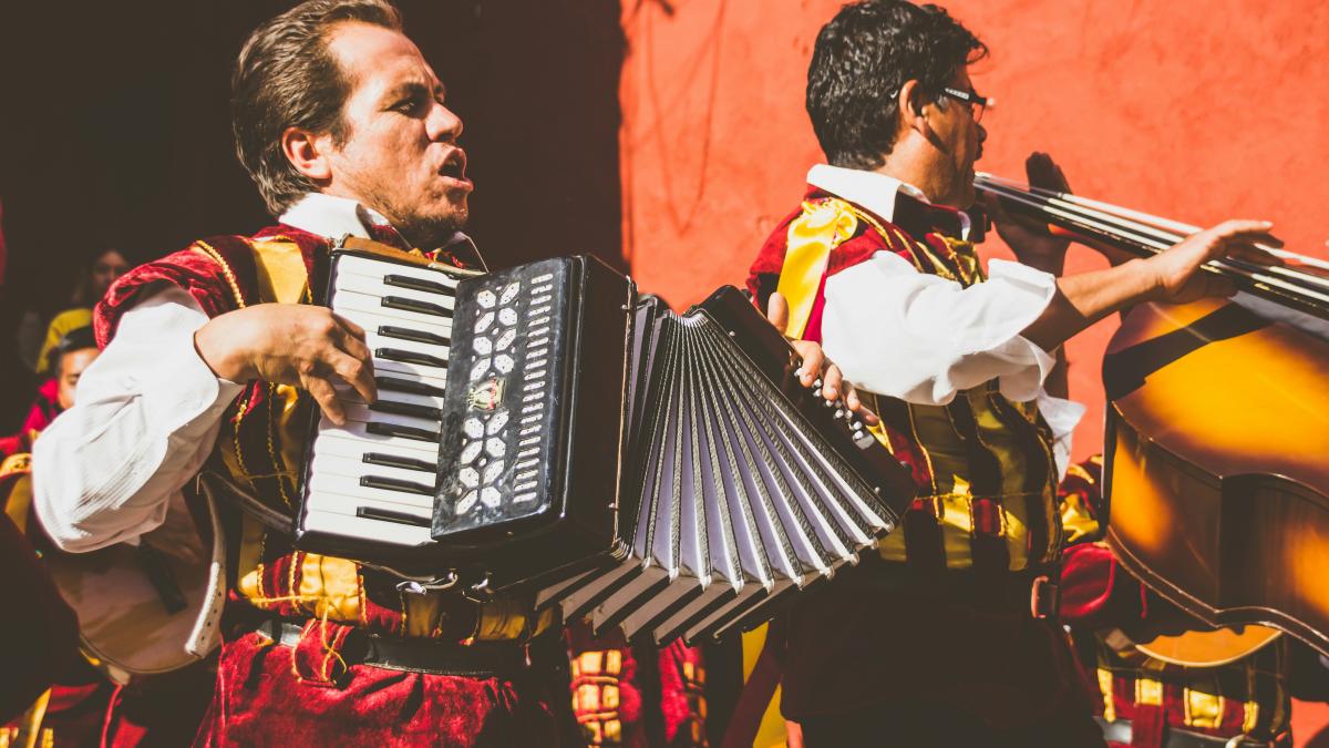 two men playing cello and accordion beside red building photo