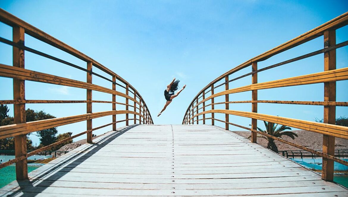 woman jumping near bridge during daytime