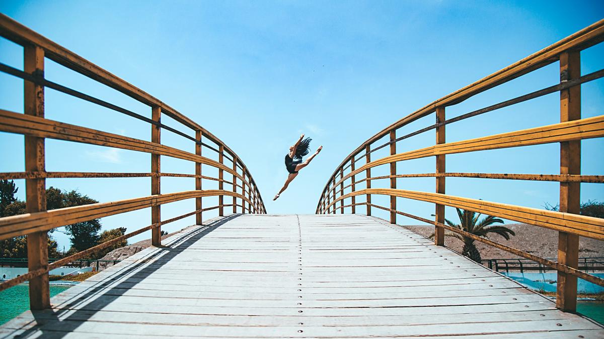 woman jumping near bridge during daytime