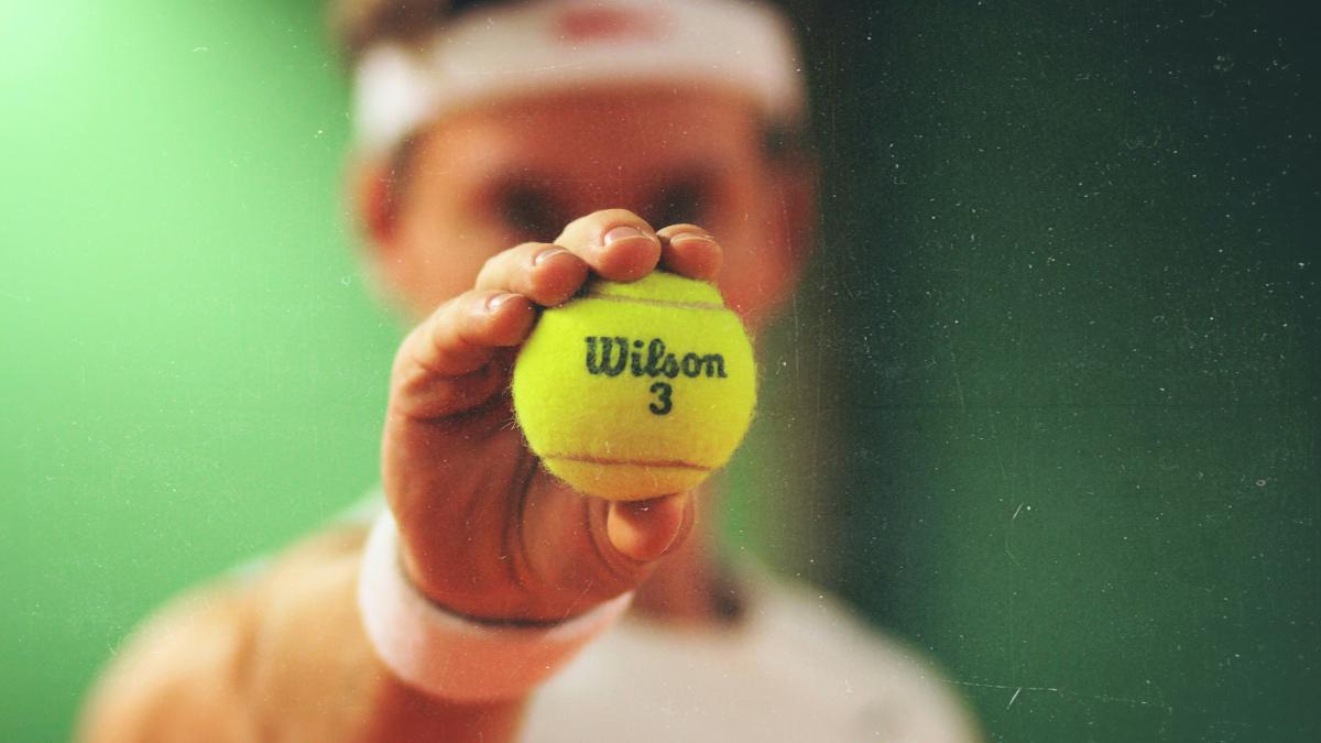 person holding green Wilson tennis ball