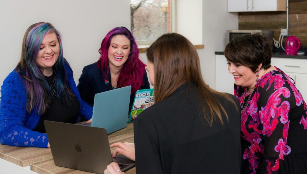 four woman on brown wooden table looking at laptops