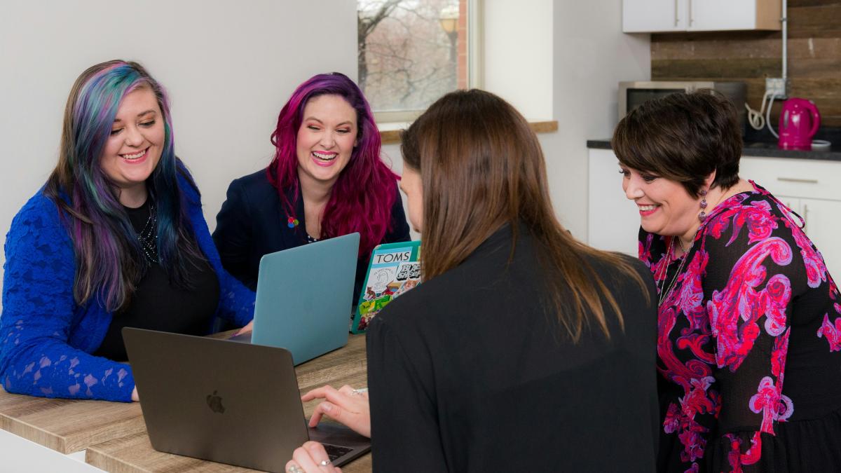 four woman on brown wooden table looking at laptops
