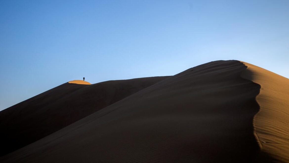 person standing on sand hill