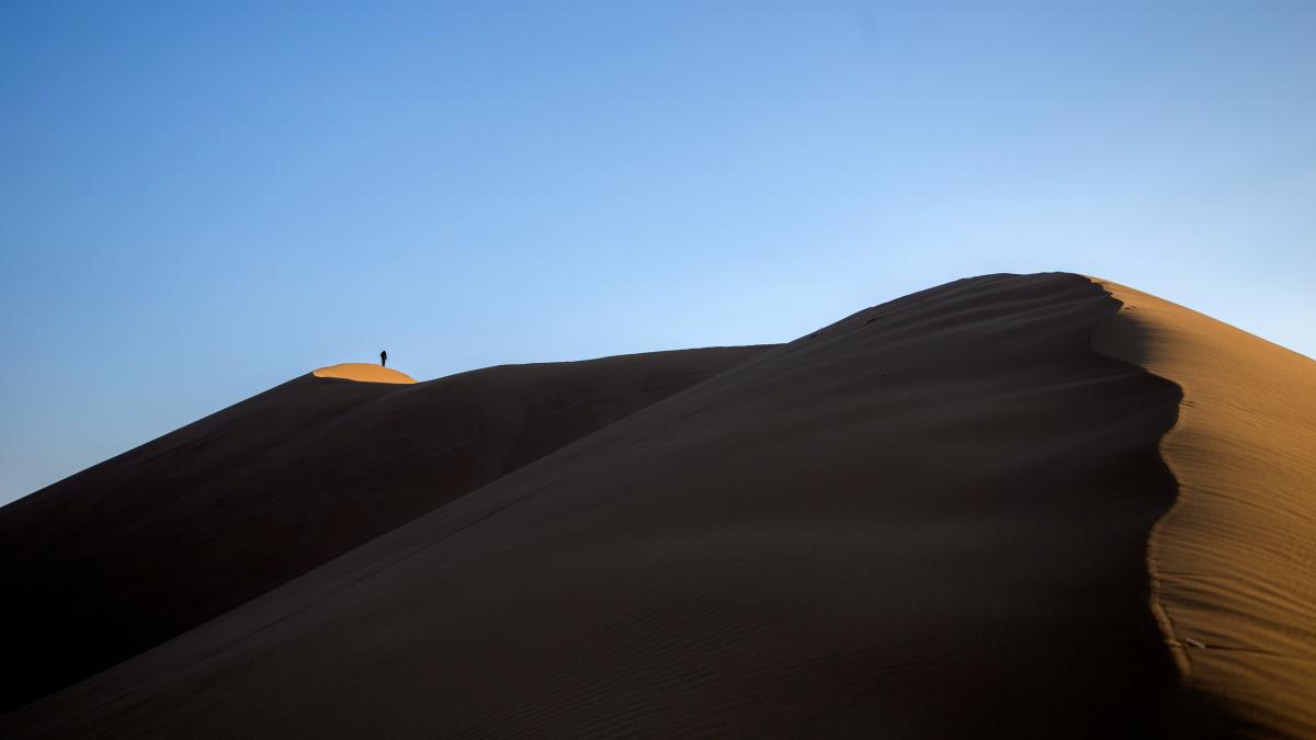 person standing on sand hill