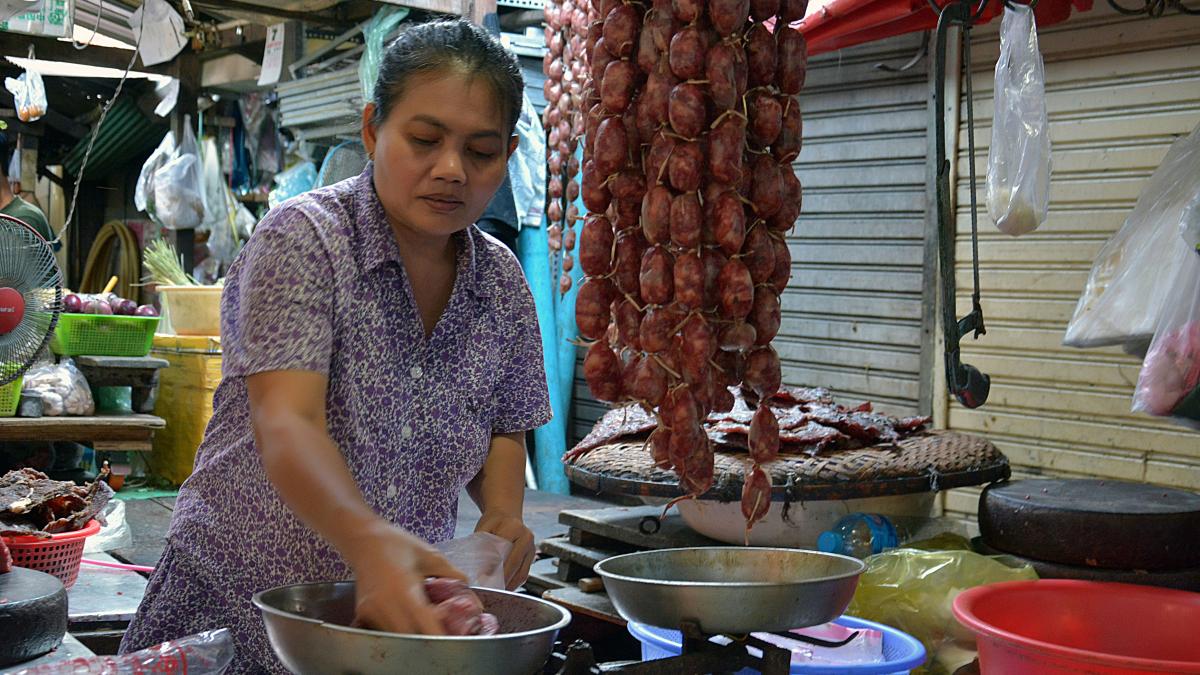 woman in blue and white polka dot shirt standing near raw meat