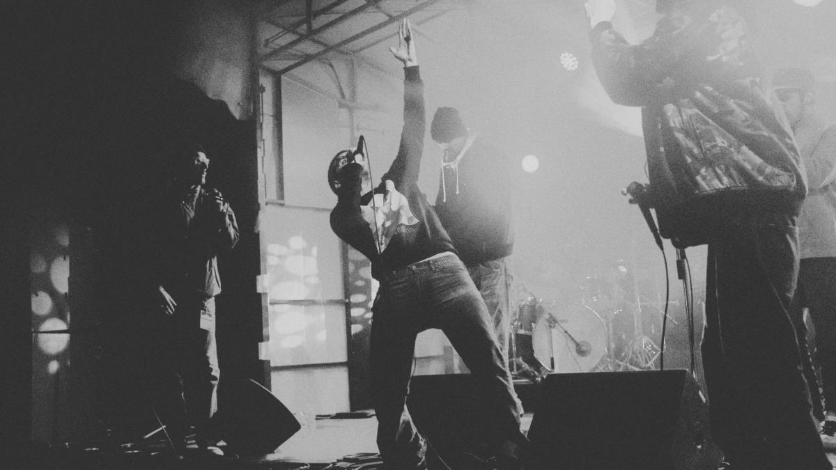 man in black jacket and denim jeans singing on stage