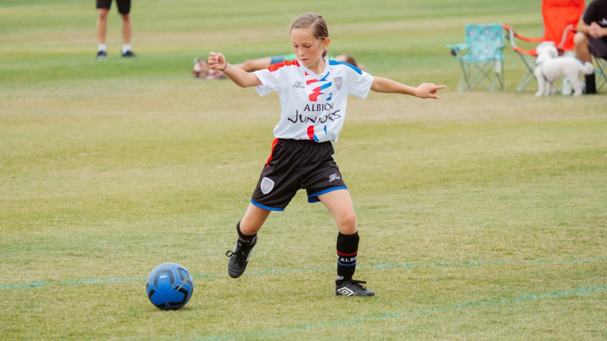 girl in white shirt and black shorts playing soccer on green grass field during daytime