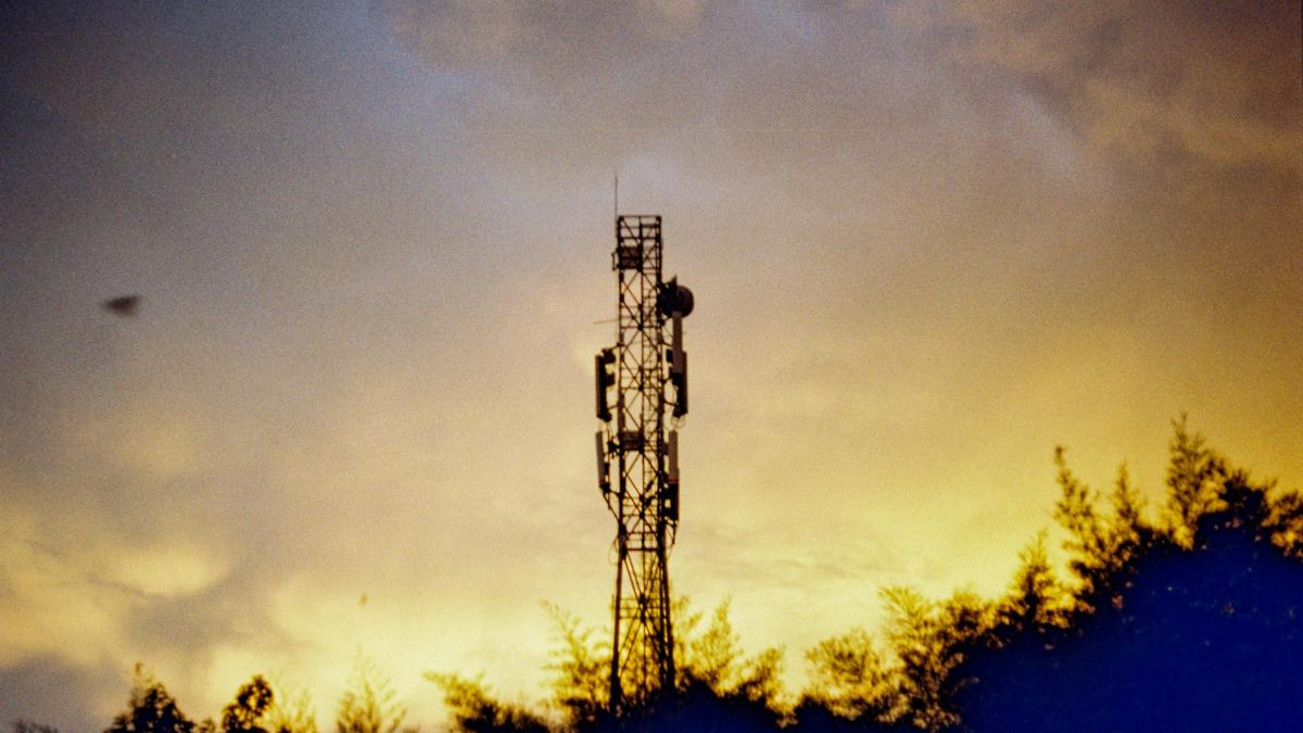 a cell phone tower is silhouetted against a cloudy sky