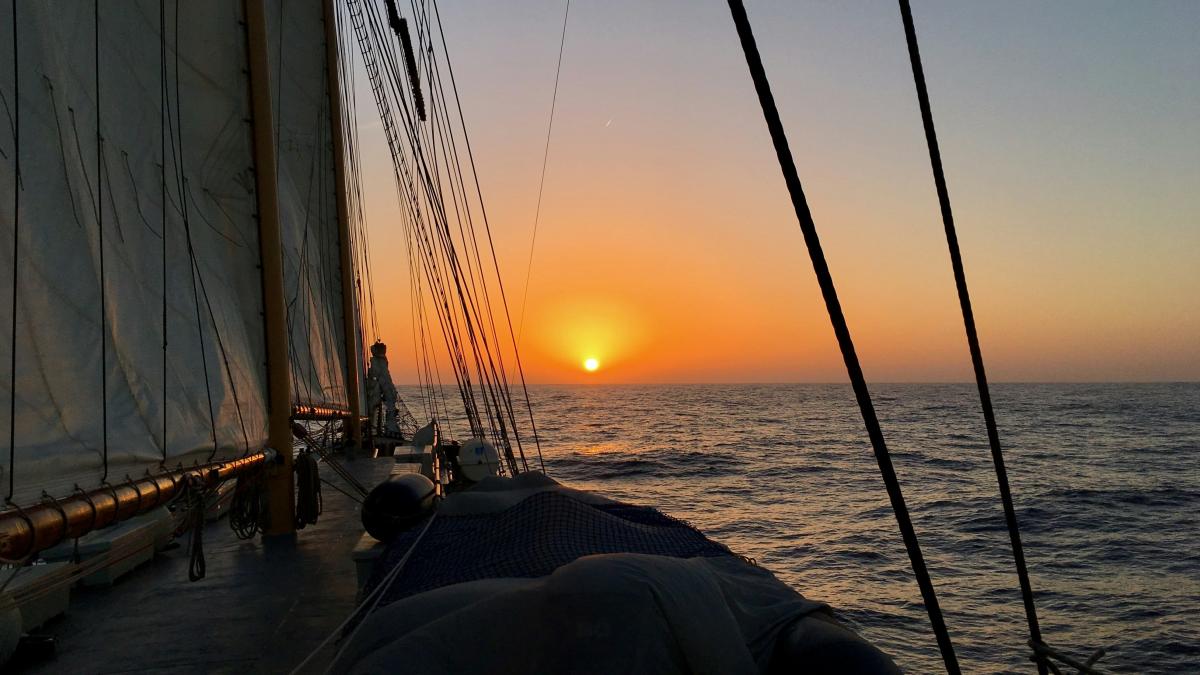 the sun is setting over the ocean on a sailboat