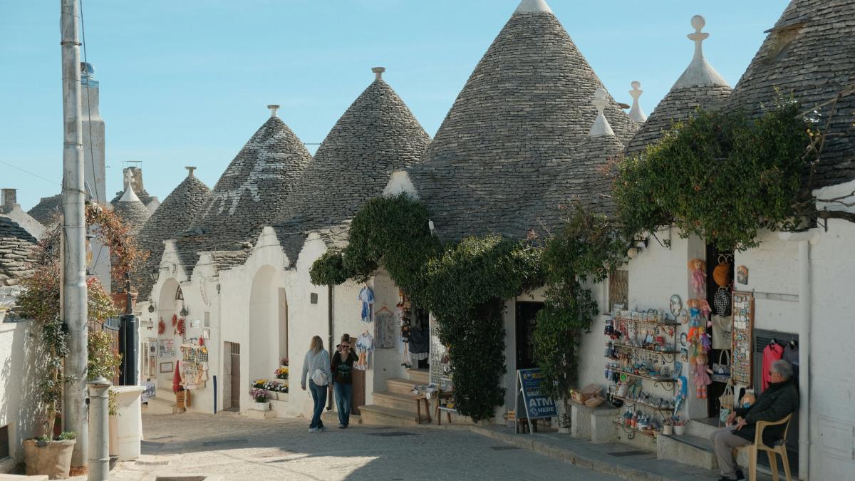 a group of people walking down a street next to white buildings