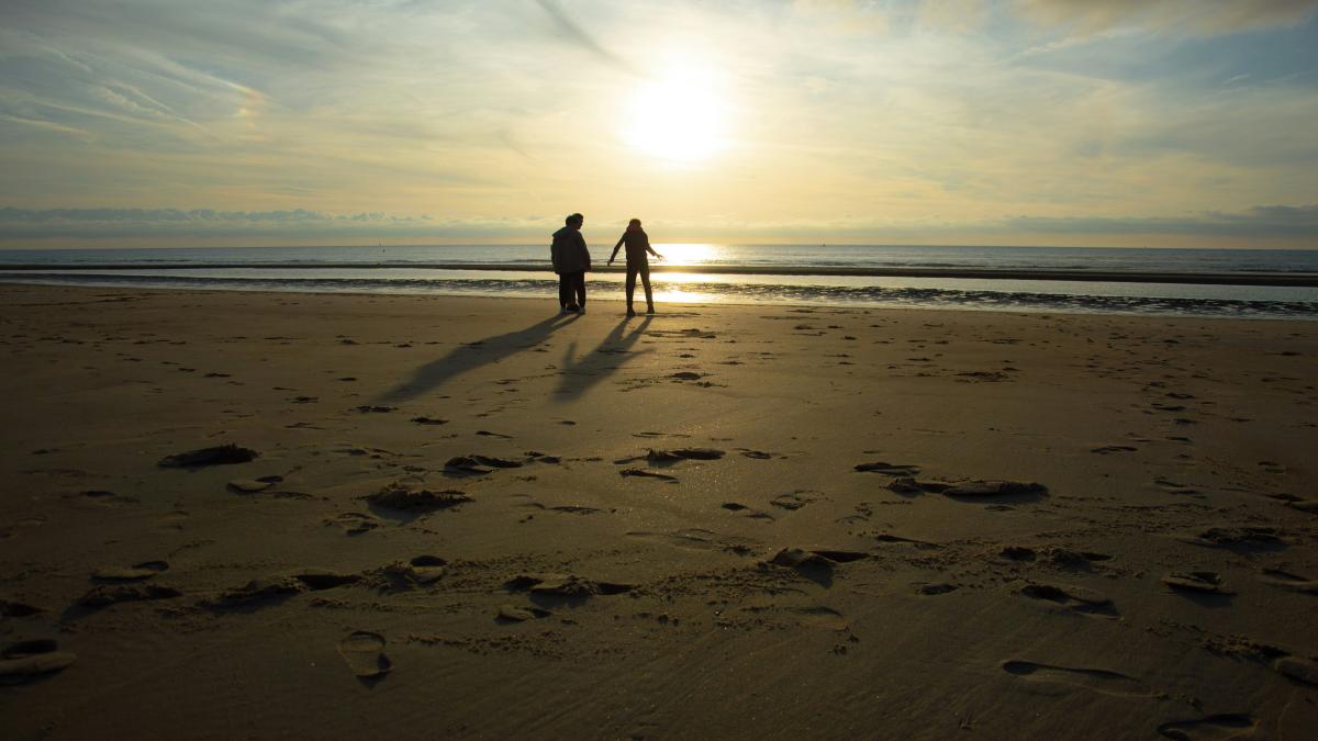 two people standing on a beach at sunset