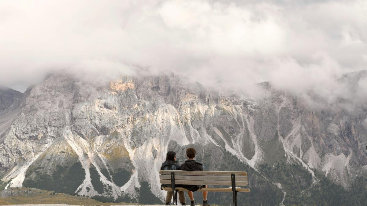 Two people sitting on a bench in front of a mountain