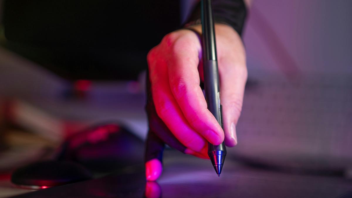 A person holding a pen and writing on a laptop
