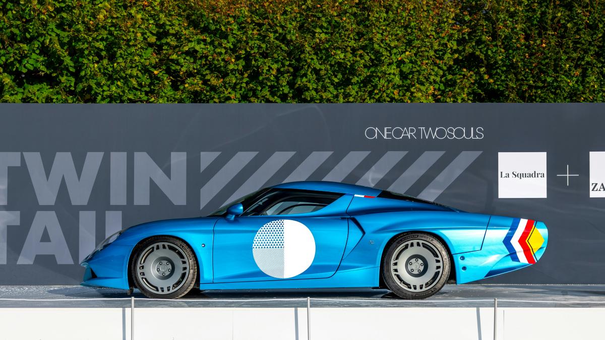 A blue sports car stands in front of a backdrop.