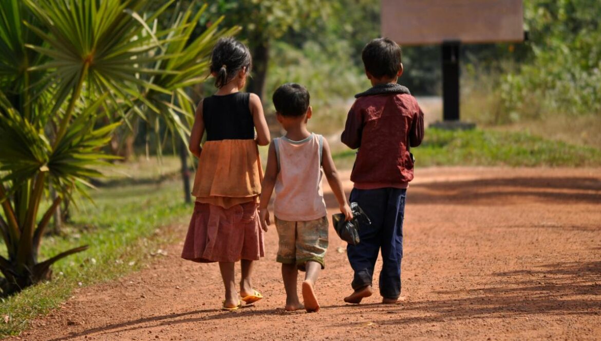 Three children walk along a dirt path.