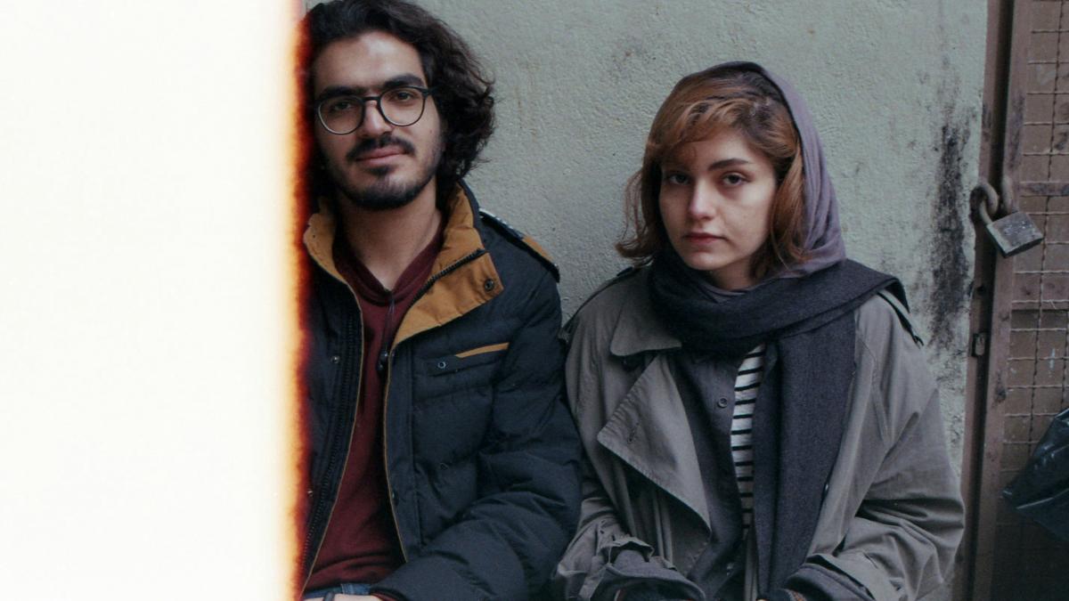 A couple sits in front of a grungy backdrop.