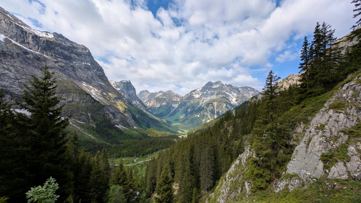 Mountainous valley under a cloudy, blue sky.