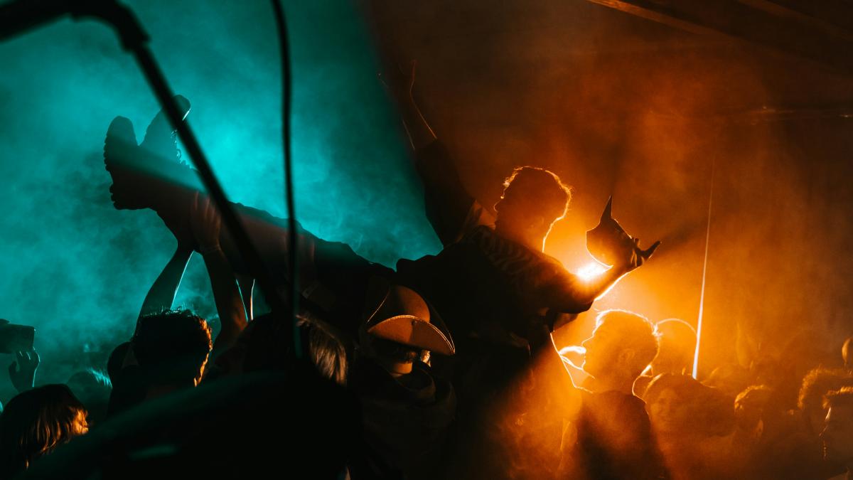 A concert crowd surfs under colorful lights.