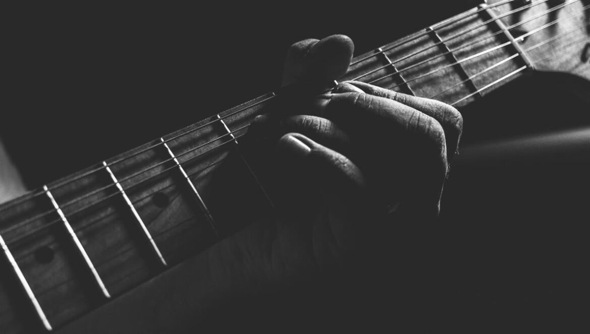 grayscale photo of person holding guitar neck and strings