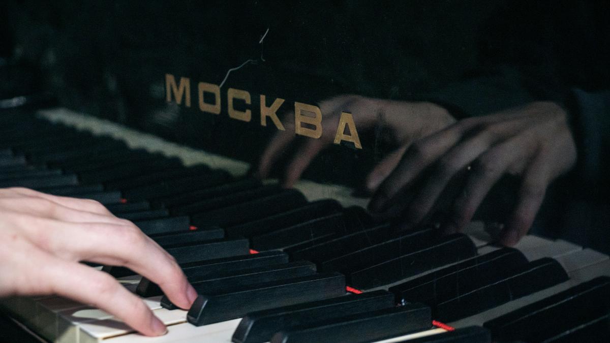 Hands are playing a piano with the name "москва."