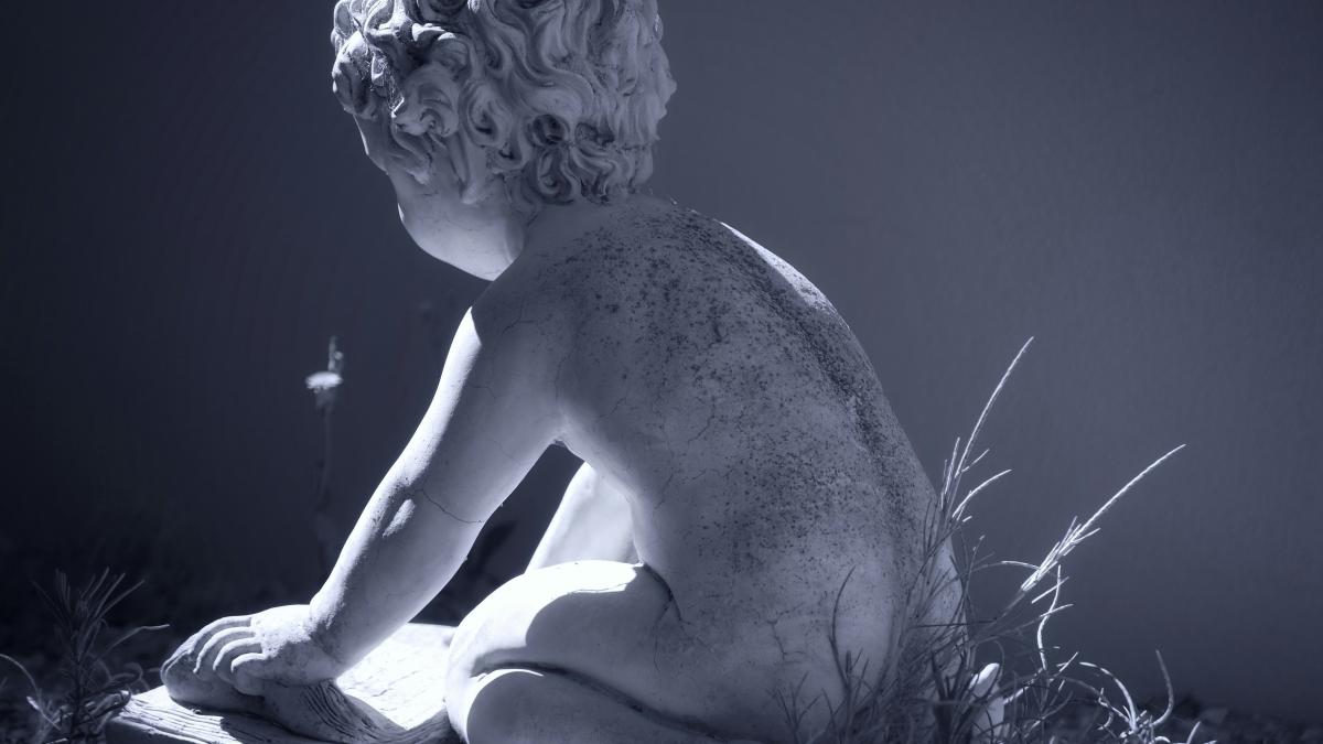 Statue of a child reading a book outdoors.