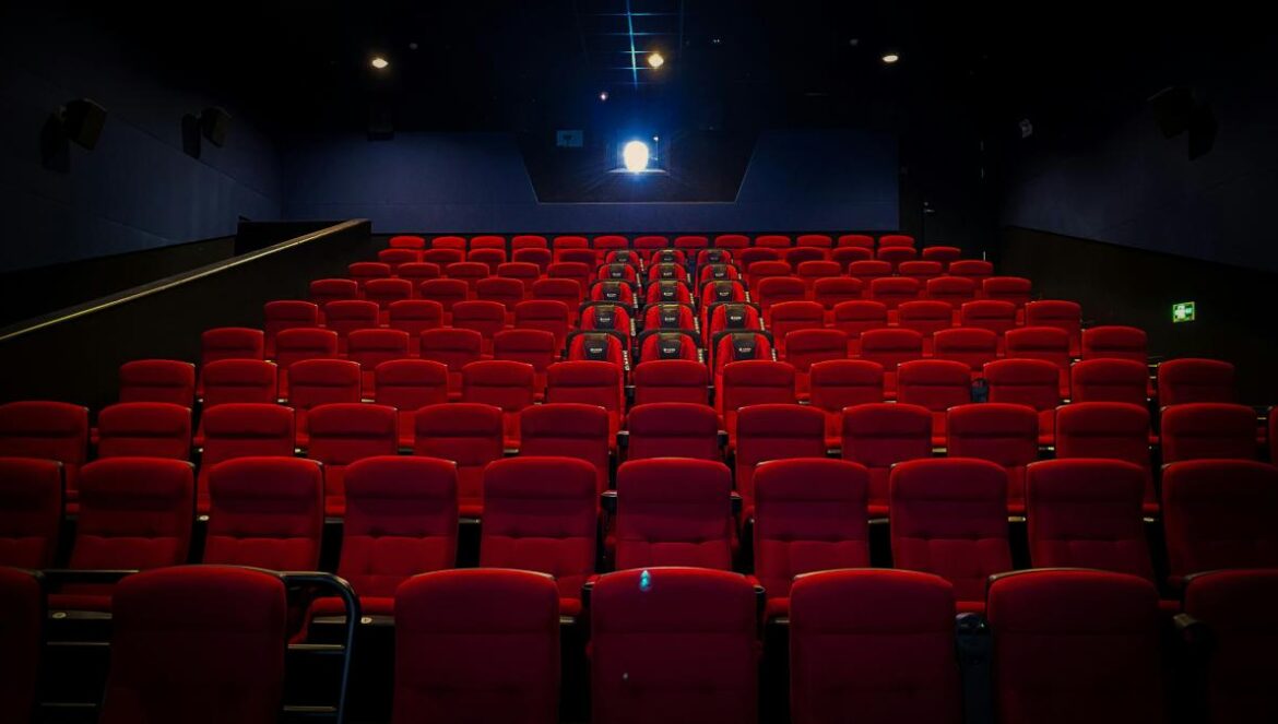 an empty theater with red seats and a projector screen