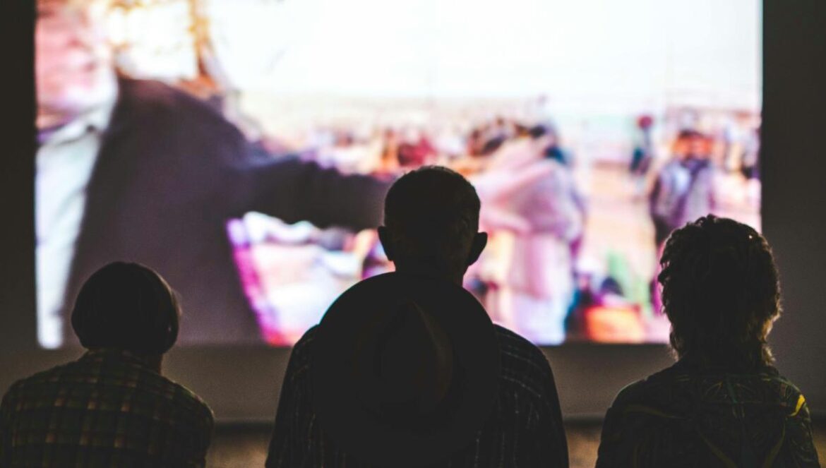 silhouette of 3 people watching show on TV